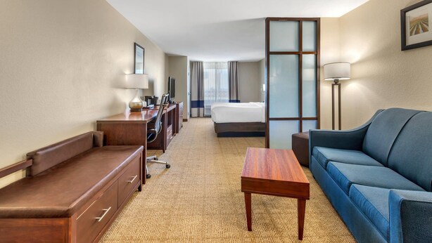 A hotel room with a bed, a sofa, a desk, a chair, a lamp, and a TV. - Comfort Suites Blythe (Blythe)