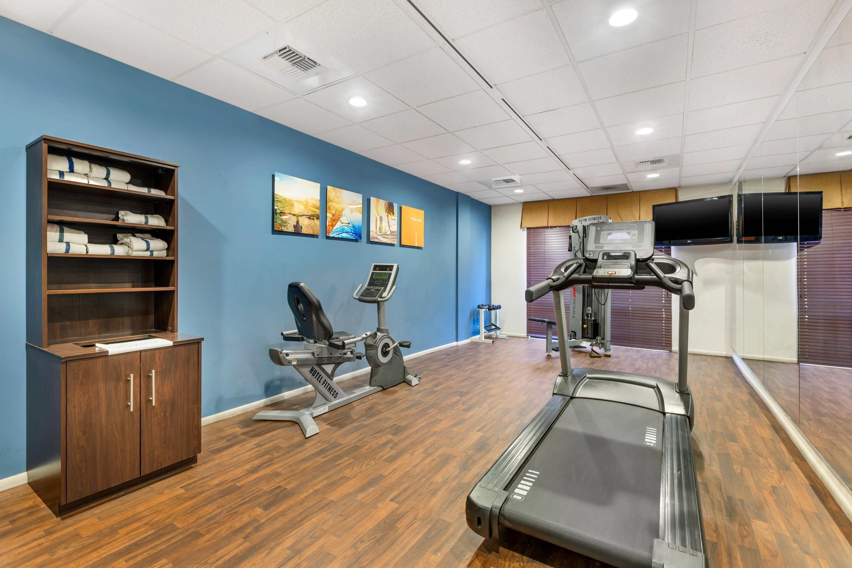 A fitness center with exercise equipment, a treadmill, and a cabinet with towels.