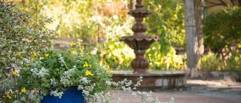 A garden with a blue pot of flowers and a stone fountain.