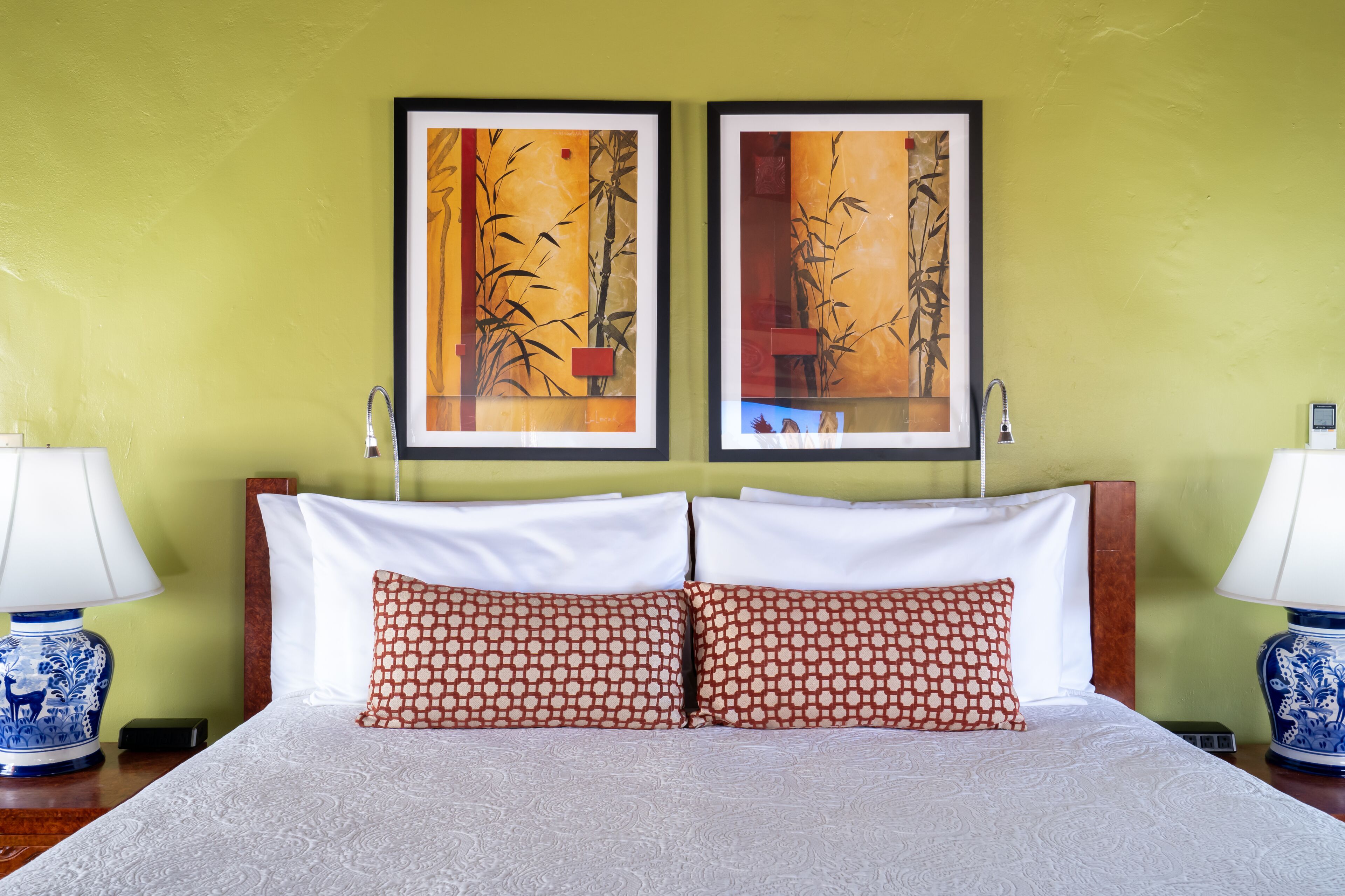 A hotel room with a bed, two pillows, two wall-mounted picture frames, and two bedside lamps.