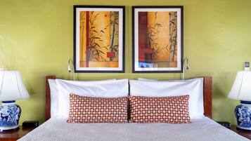 A hotel room with a bed, two pillows, two wall-mounted picture frames, and two bedside lamps.