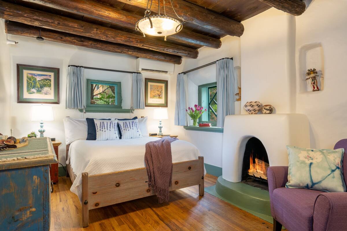 A cozy bedroom with a wooden bed, a fireplace, and a view of the outdoors.