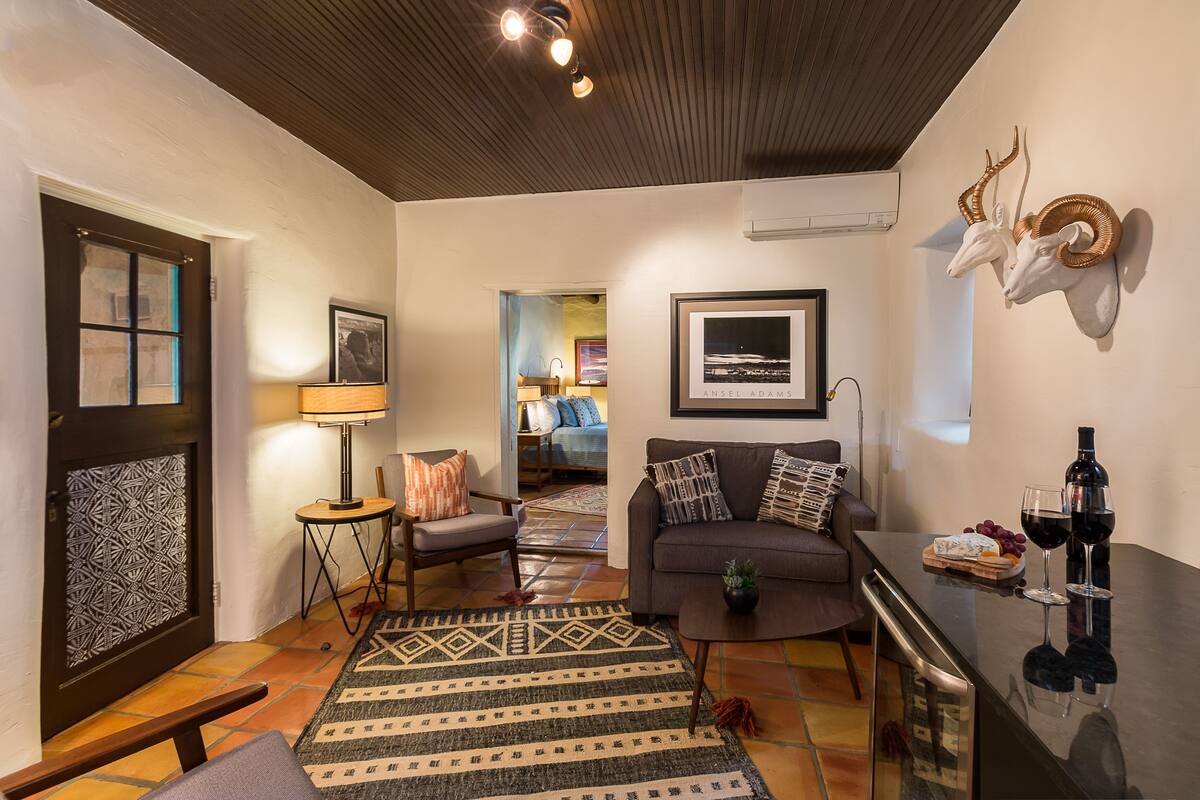 A living room with a sofa, armchair, coffee table, and a rug. There is a wine bottle and glasses on a table.