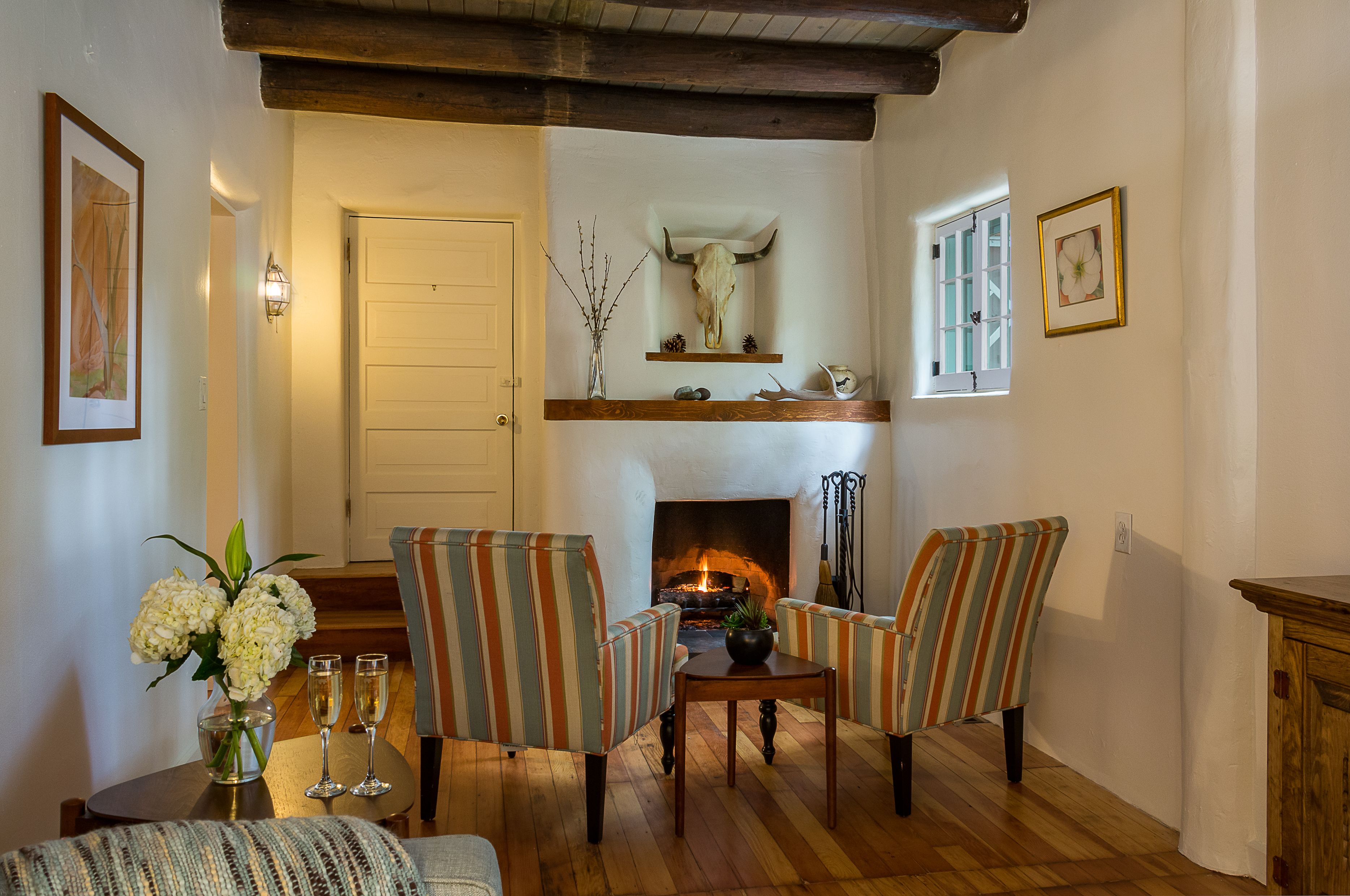 A cozy living room with a fireplace, striped armchairs, a wooden coffee table, and a vase with flowers.
