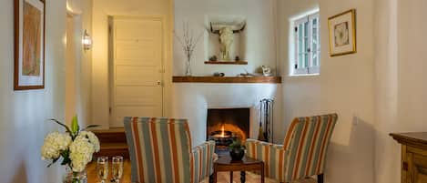 A cozy living room with a fireplace, striped armchairs, a wooden coffee table, and a vase with flowers.