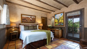 A bedroom with a large bed, wooden headboard, two bedside lamps, a nightstand, a dresser, a door leading outside, and two paintings on the walls.