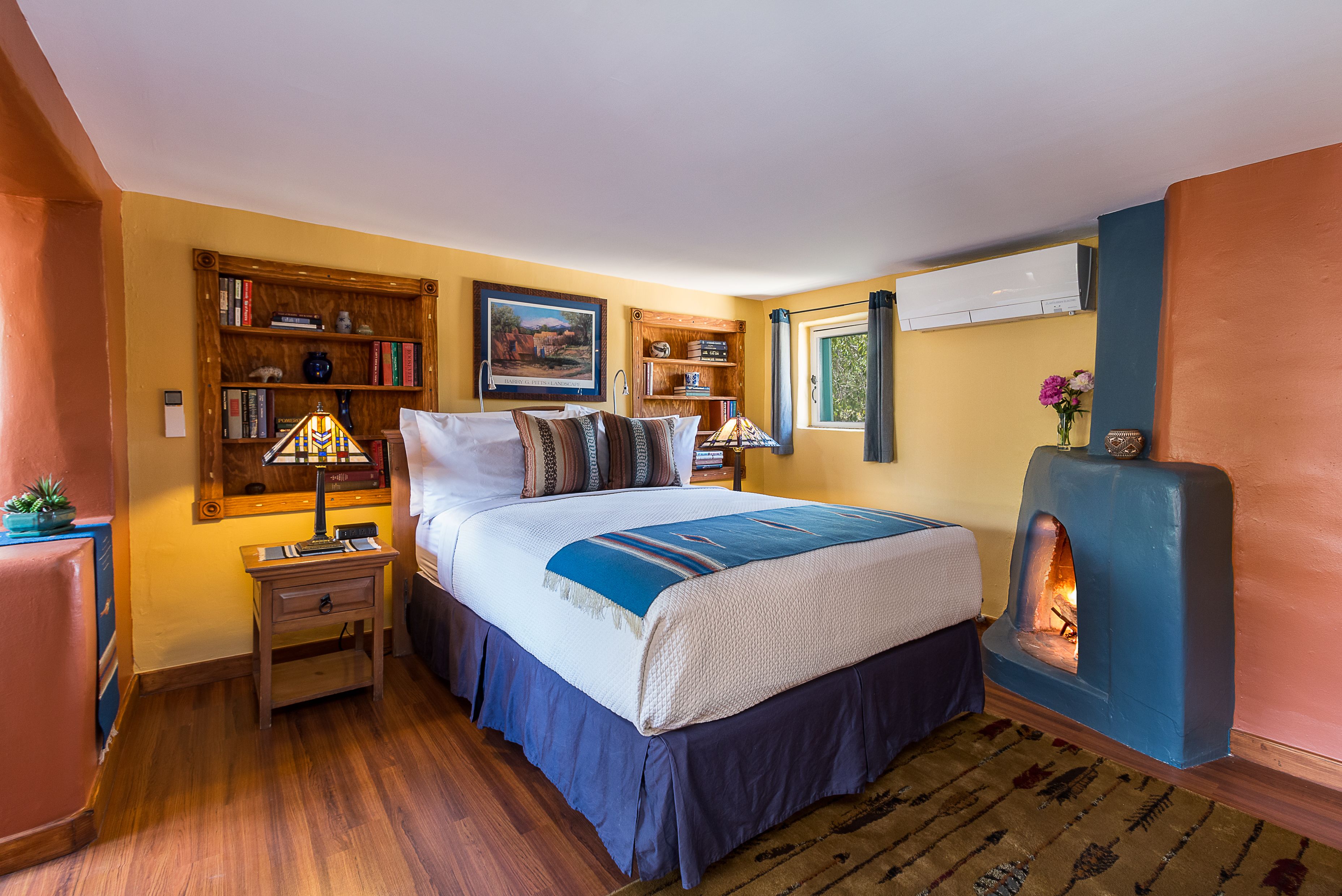 A bedroom with a bed, bedside tables, a bookshelf, a fireplace, and a window.