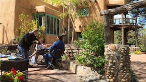 A patio area with outdoor seating, a stone wall, and a building with stucco walls and green window frames.