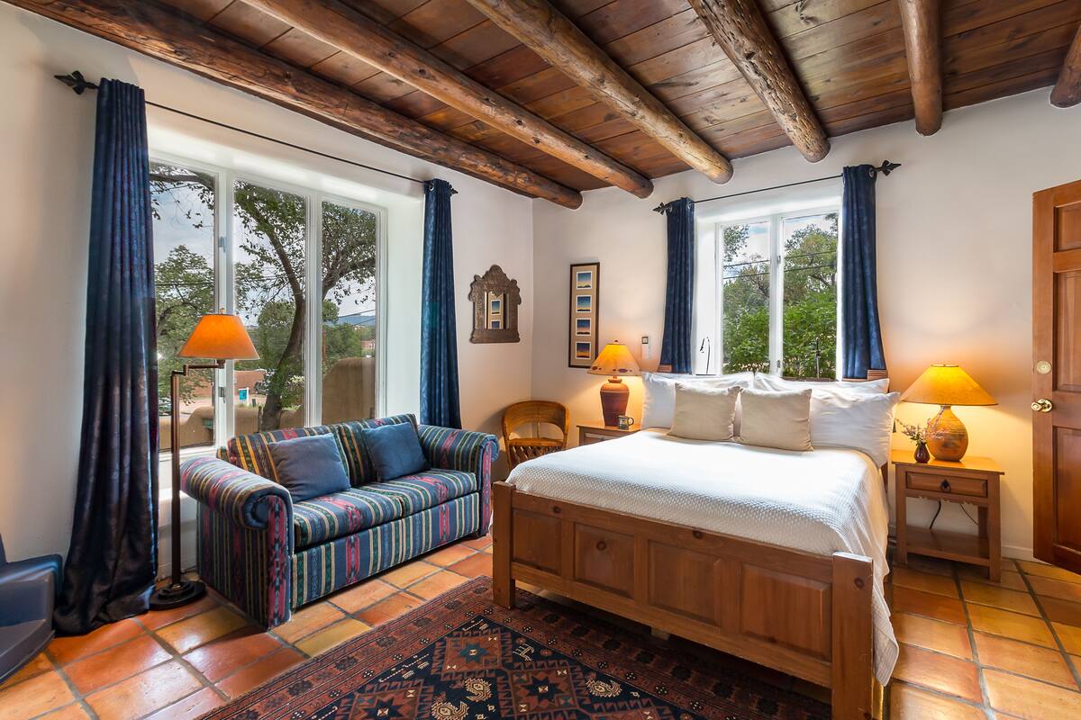 A bedroom with a wooden bed, a striped sofa, and a large window with curtains.