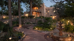 A stone pathway leading to a building with a balcony and a fountain.