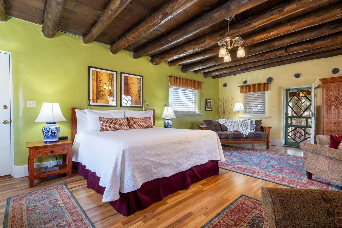 A bedroom with a large bed, wooden flooring, a wooden ceiling, and a green wall.