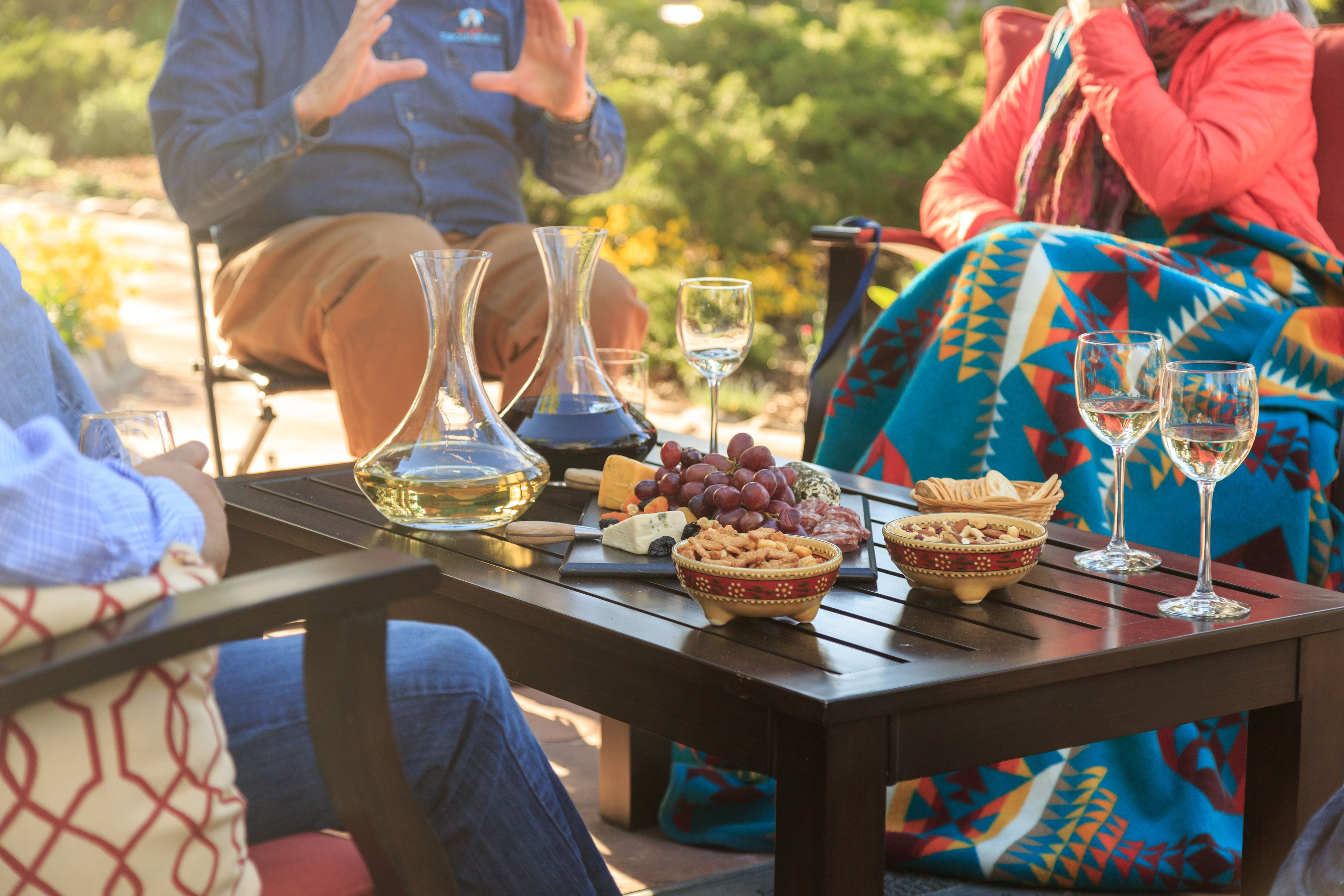 A table set outdoors with a variety of food items and two wine glasses.
