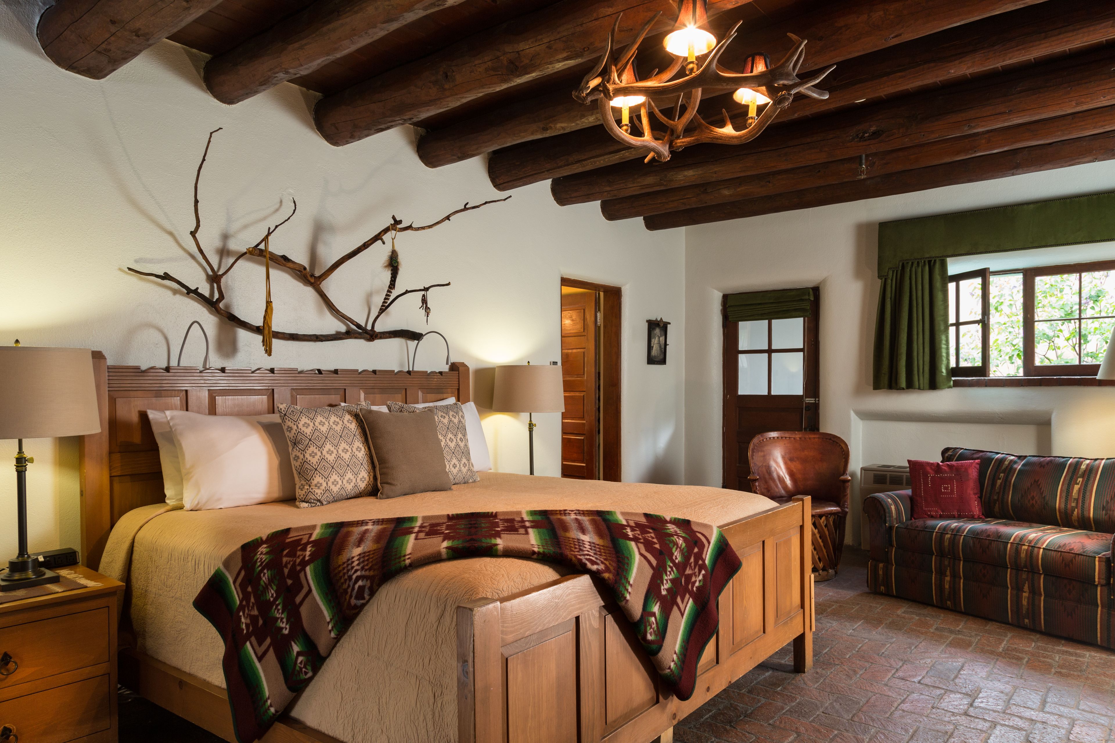 Quarto aconchegante com uma cama grande, cabeceira de madeira e uma decoração com galhos. Há um sofá e uma cadeira no canto.