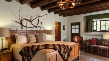 Quarto aconchegante com uma cama grande, cabeceira de madeira e uma decoração com galhos. Há um sofá e uma cadeira no canto.