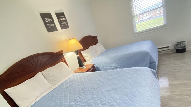 A room with two beds, a nightstand with a lamp, a window with blinds, and a wall with two framed items. - Relax Inn Smyrna (Smyrna)