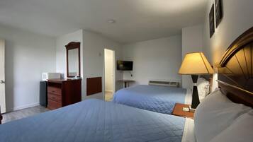 A hotel room with two beds, a TV, a desk, a dresser, and a lamp.