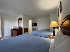 Quarto de hotel com duas camas, televisão, escrivaninha, cômoda e abajur.