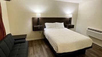 A hotel room with a bed, two bedside tables with lamps, a sofa, and a wall-mounted heater.