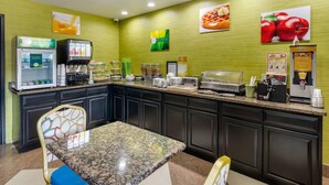 A hotel kitchen with a granite countertop, a coffee machine, a waffle maker, and a refrigerator.