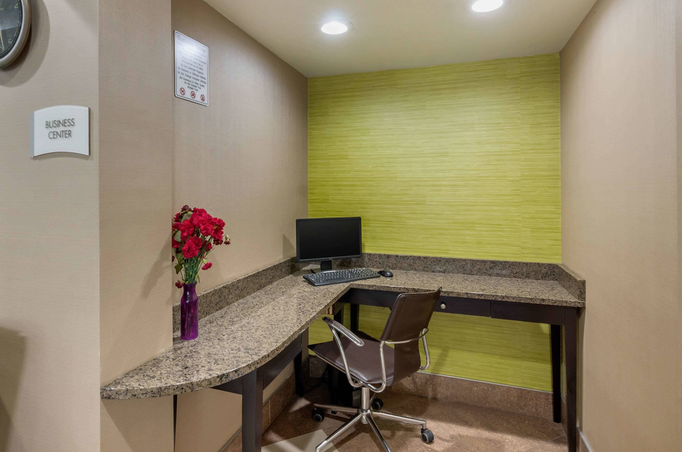 Un centro business con scrivania, sedia, computer e un vaso di fiori.
