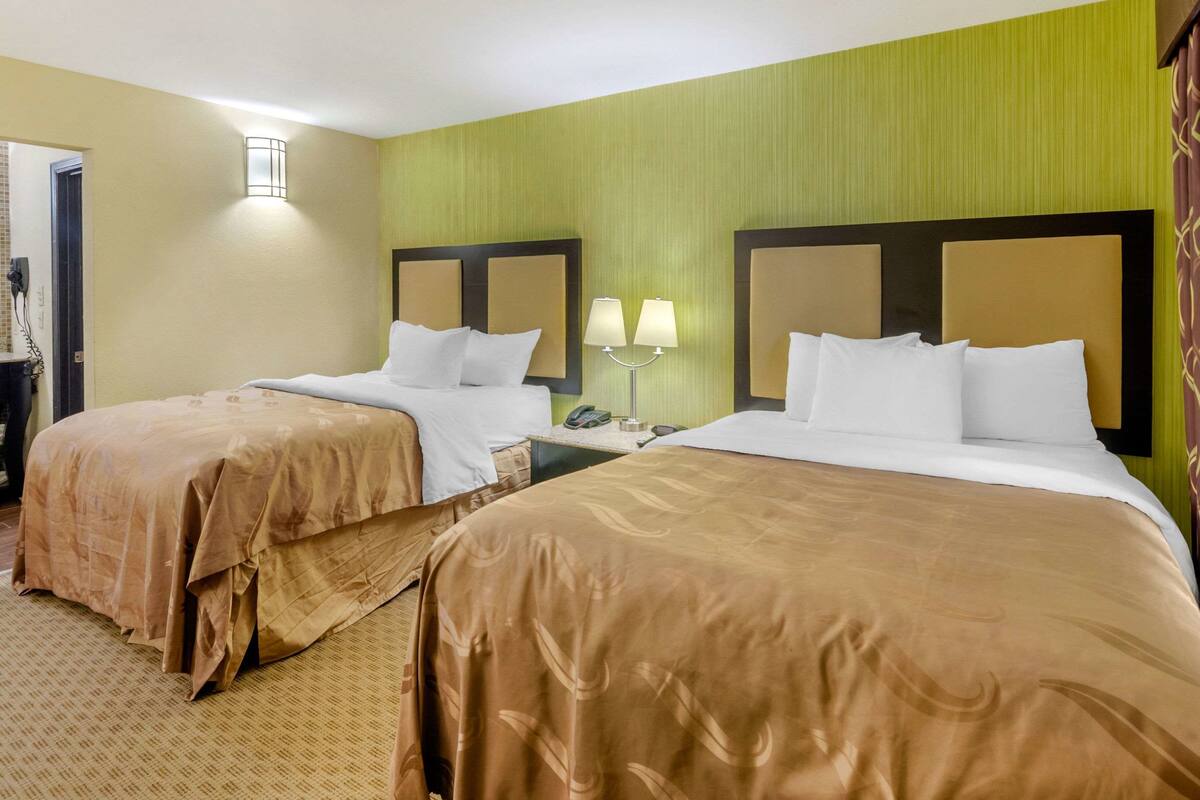 Quarto de hotel com duas camas, cada uma com cabeceira e mesa de cabeceira com abajur.