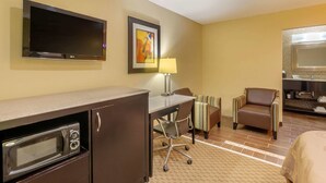 A hotel room with a flat-screen TV, a desk with a lamp, a microwave, a striped armchair, and a bed.