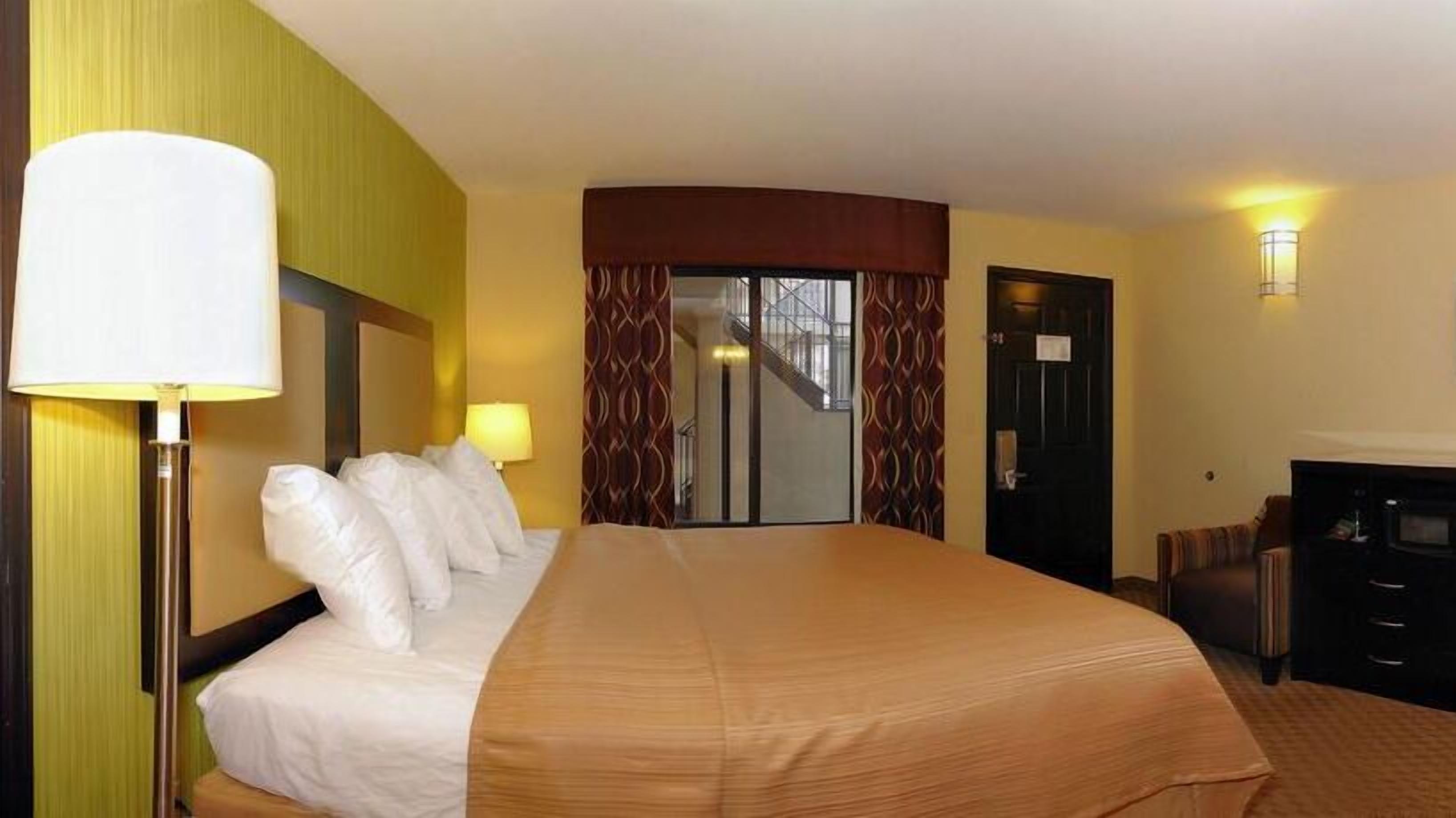 Una habitación de hotel con una cama grande, dos lámparas de noche, un escritorio y una puerta que da a una escalera.