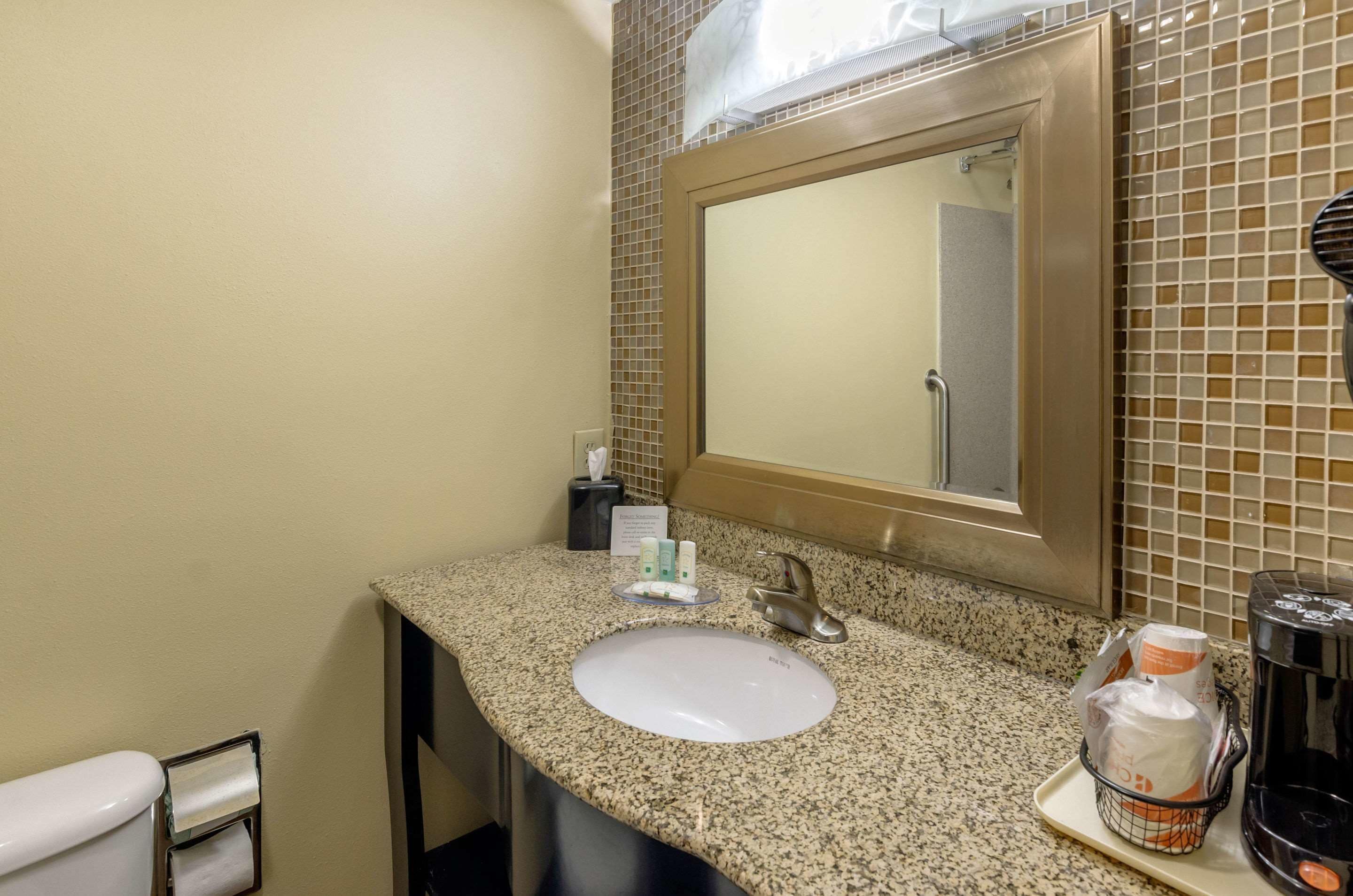 A bathroom with a granite countertop, a white sink, a mirror, and toiletries.