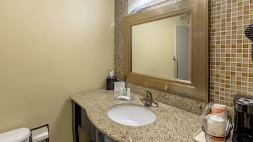 A bathroom with a granite countertop, a white sink, a mirror, and toiletries.
