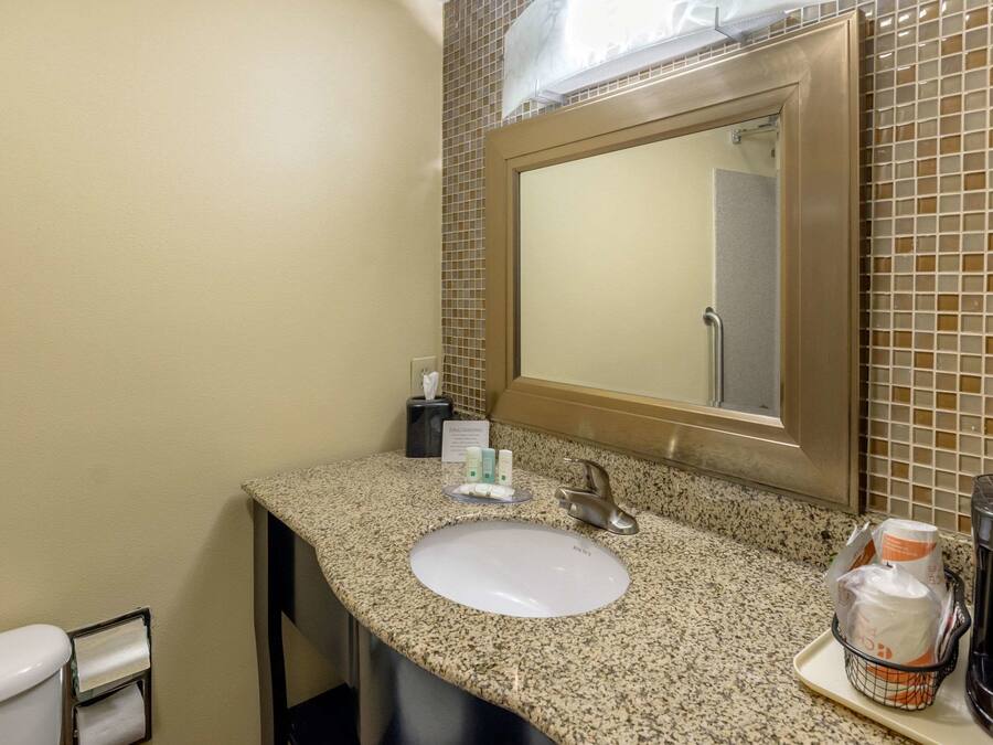 A bathroom with a granite countertop, a white sink, a mirror, and toiletries.
