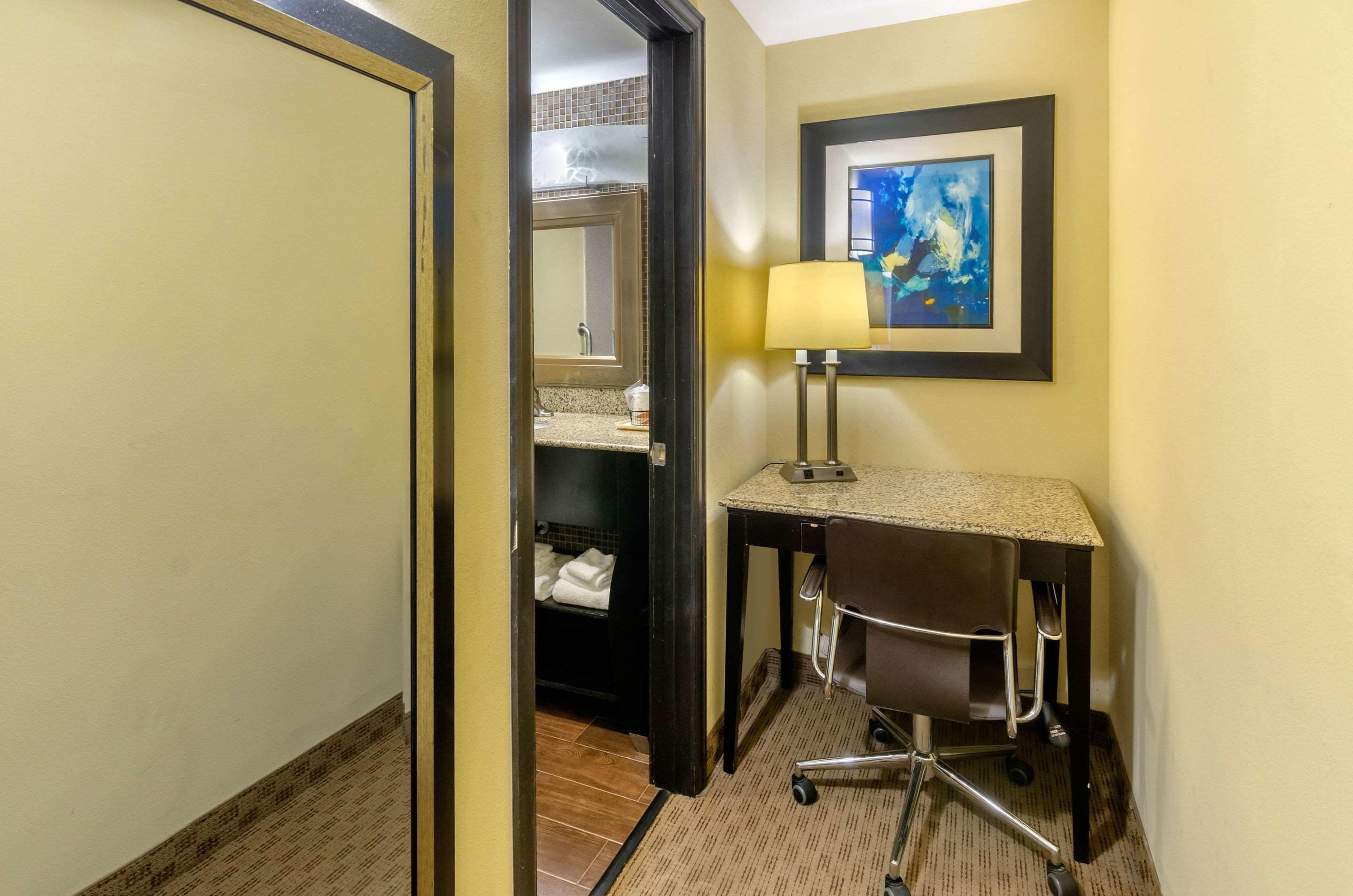 A hotel room with a desk, chair, and a framed abstract painting on the wall.