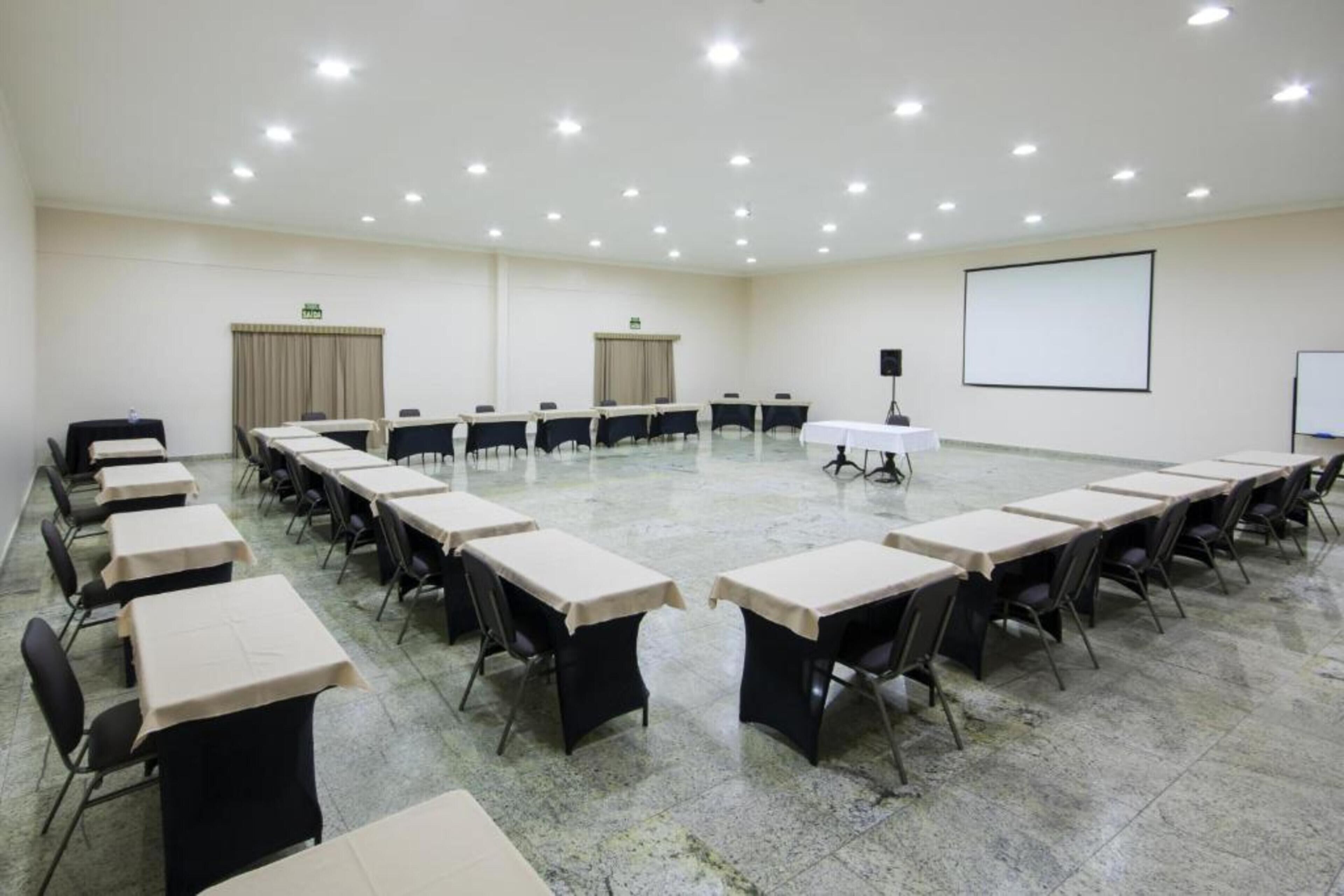 A conference room with multiple tables and chairs, a projector screen, and a whiteboard.