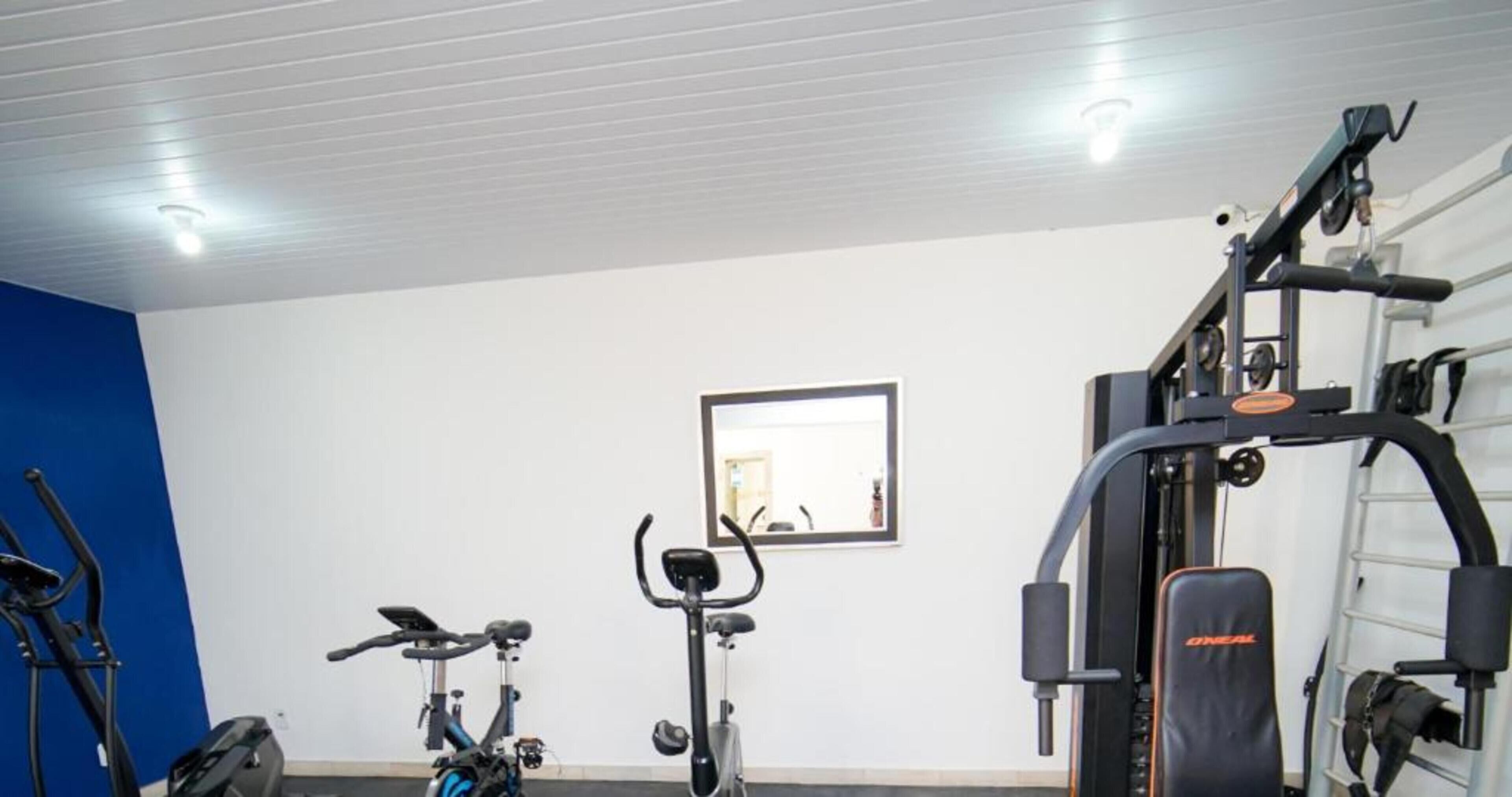 Un gimnasio con equipo de ejercicio, incluyendo una elíptica, una bicicleta estática y una máquina de pesas.