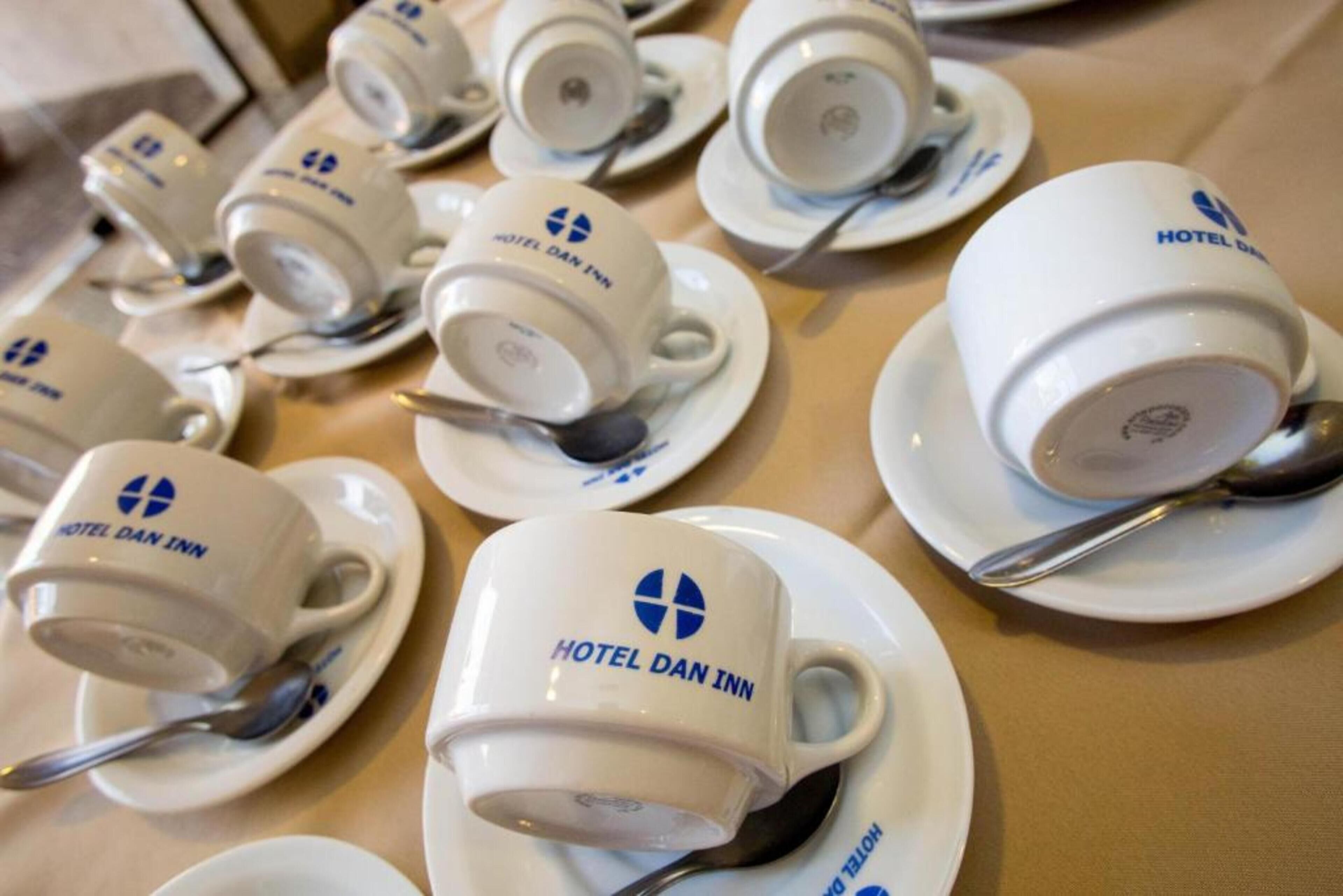 Een tafel met meerdere witte kopjes en schoteltjes, elk met het logo van Hotel Dan Inn.