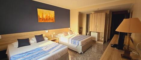 A hotel room with two beds, a painting on the wall, a desk with a lamp, and a wardrobe.
