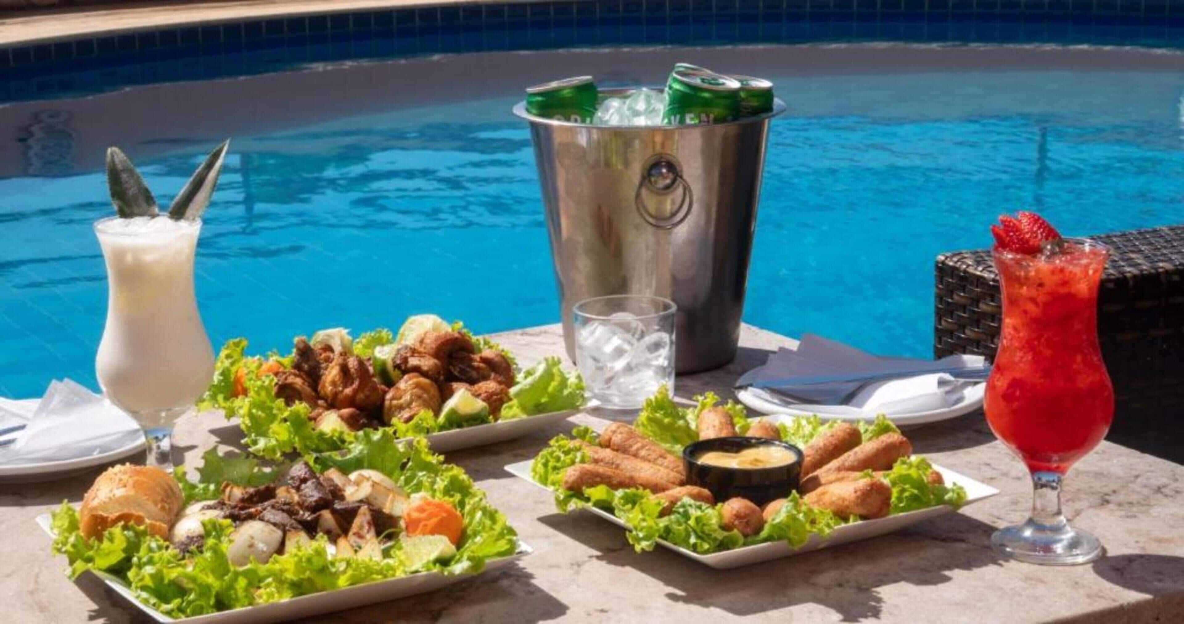 Mobiliario de comedor junto a la piscina con diversos platos, bebidas y un cubo.