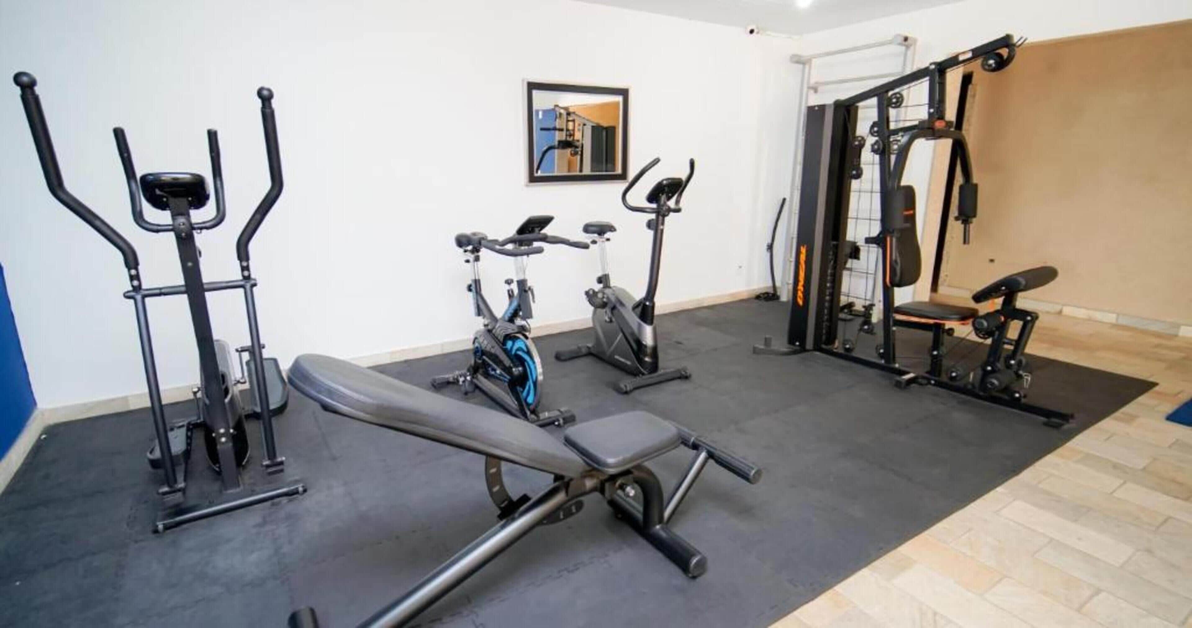 A gym with various exercise equipment including a bench, elliptical, and weight machines.