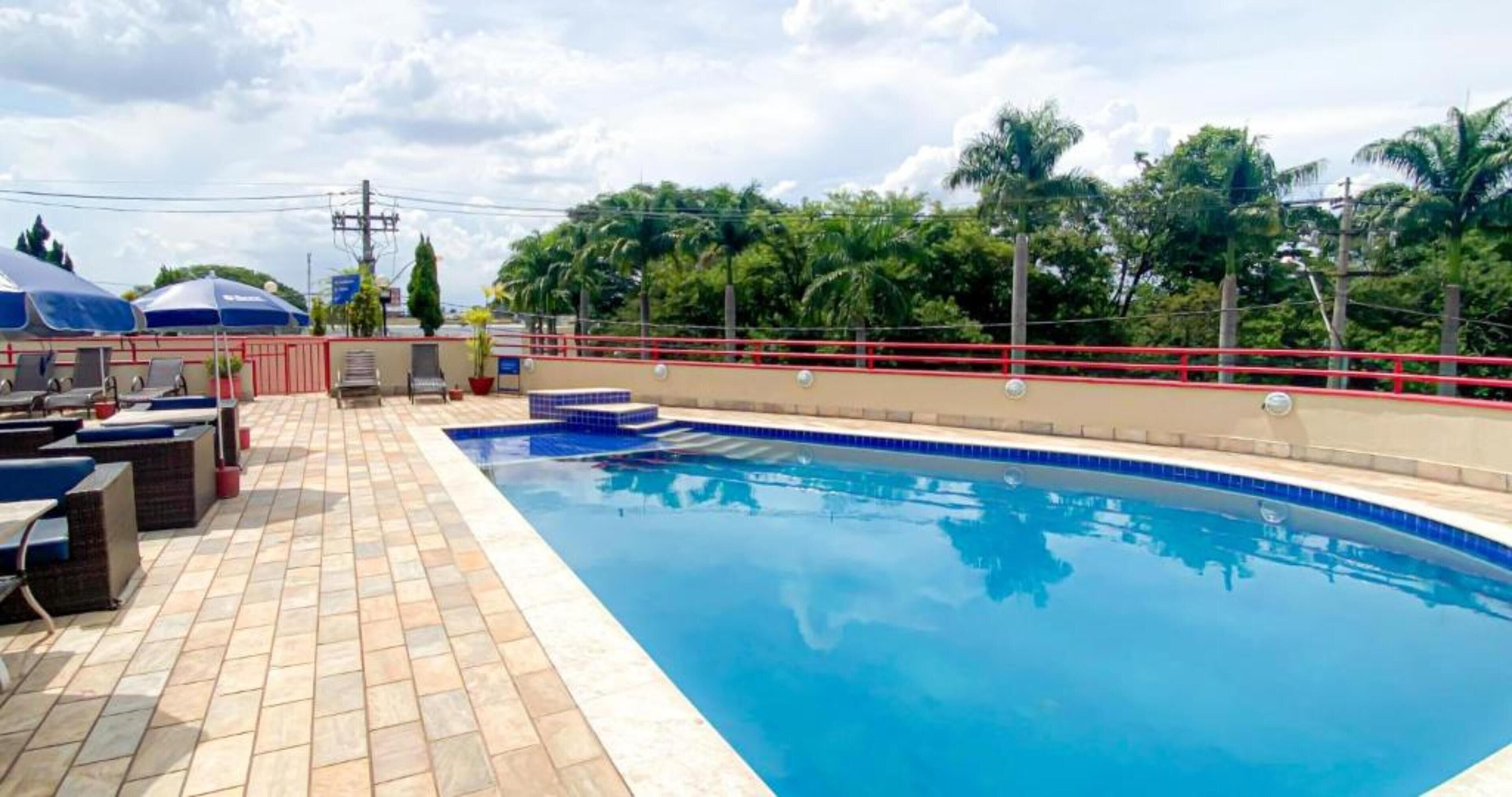Une piscine dotée d’une terrasse carrelée, de garde-corps de sécurité rouges et de mobilier d’extérieur.