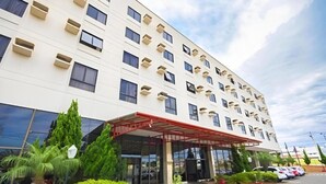 A multi-story hotel with a modern design, featuring a covered entrance and a parking area with several cars.