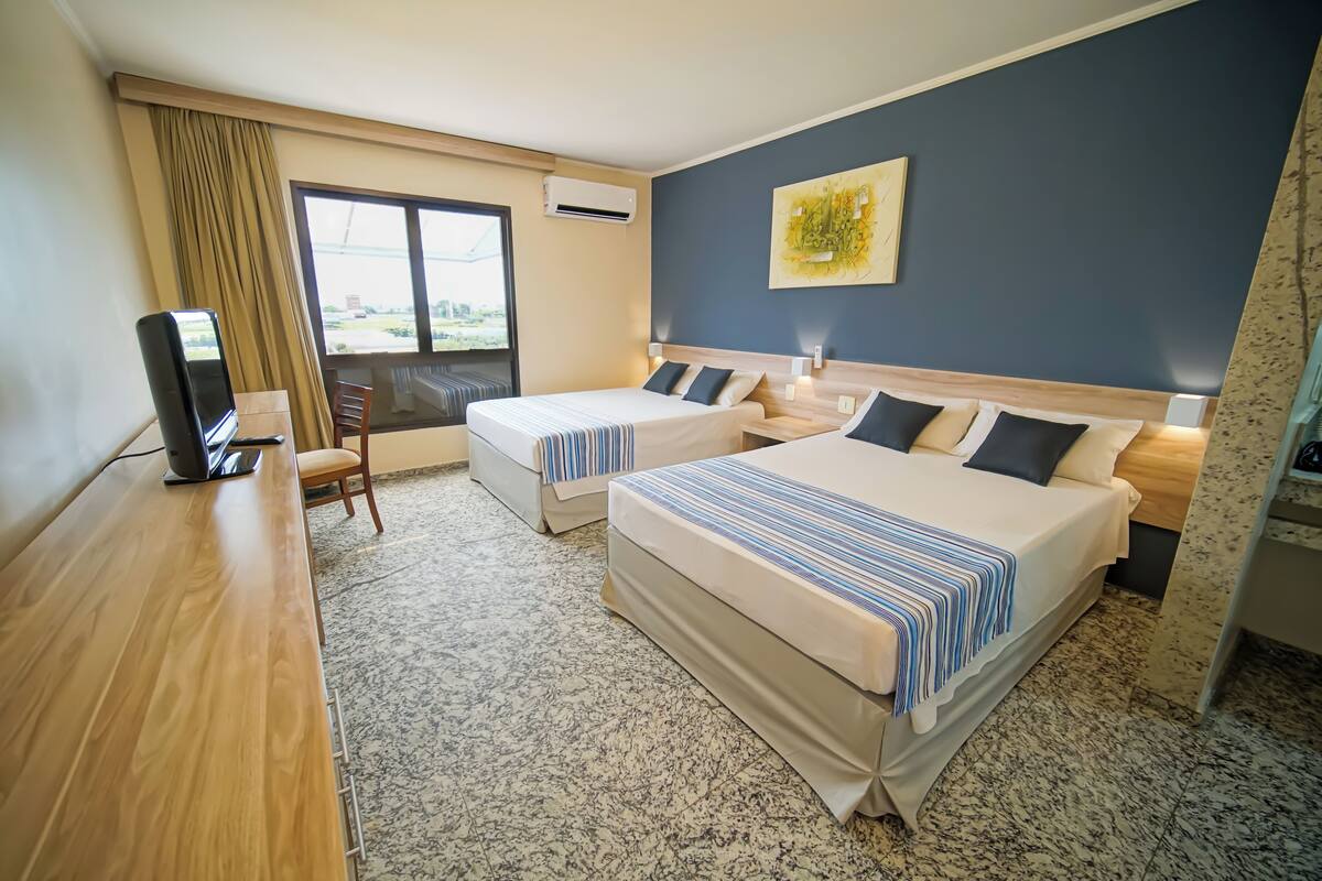 A hotel room with two beds, a desk, a chair, and a large window.