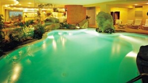A swimming pool with a greenish hue, surrounded by lounge chairs and potted plants.