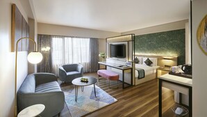 A modern hotel room with a sofa, armchair, desk, and a television. - Hotel Suba International (Mumbai)