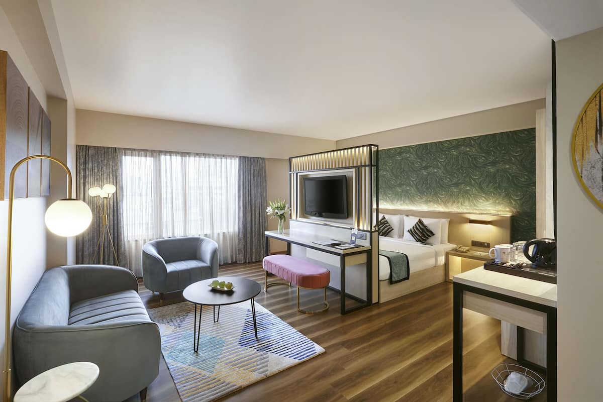 Una habitación de hotel moderna con sofá, sillón, escritorio y televisor.