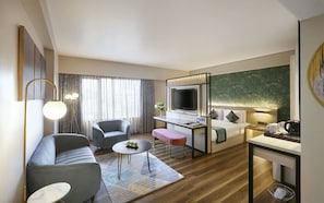 A modern hotel room with a sofa, armchair, desk, and a television. - Hotel Suba International (Mumbai)