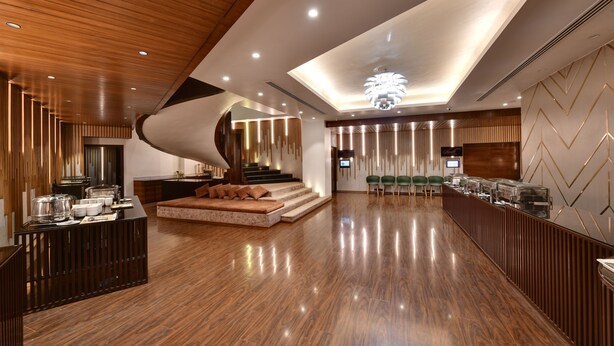 A modern hotel lobby with a wooden floor, a curved staircase, a seating area, and a buffet. - Hotel Suba International (Mumbai)