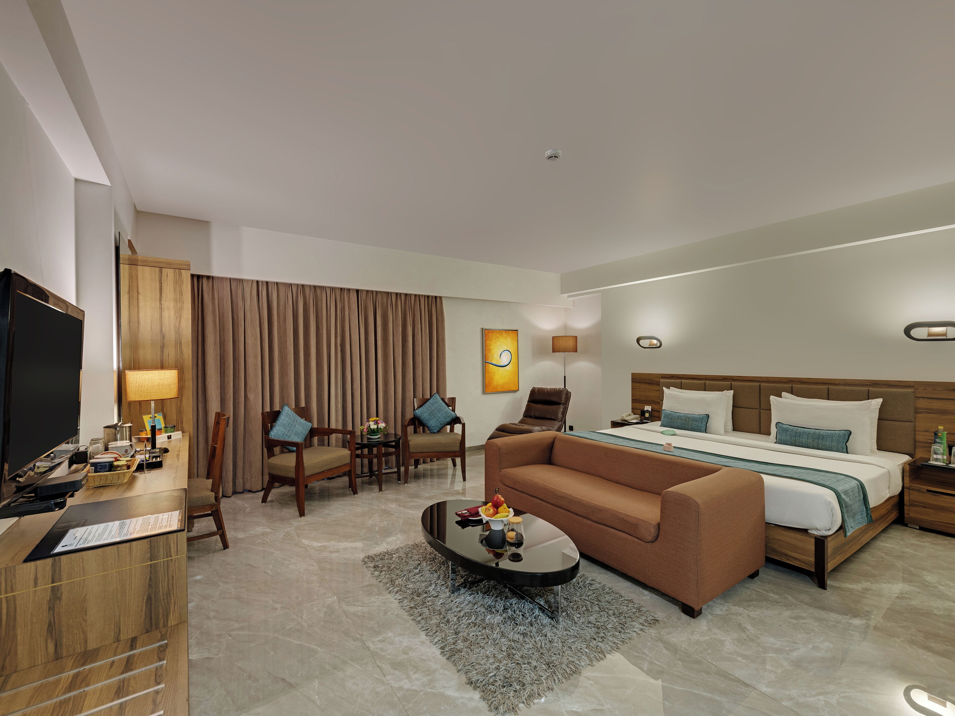 A hotel room with a bed, a sofa, a coffee table, a TV, and a desk with a computer.