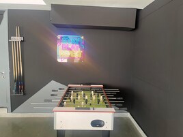 A foosball table in a room with a neon sign that reads 'STAY PLAY REPEAT.'