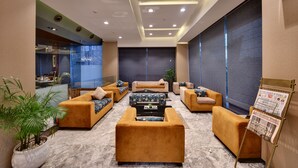 A lobby with sofas, a coffee table, a potted plant, and a newspaper stand. - Hotel Suba International (Mumbai)