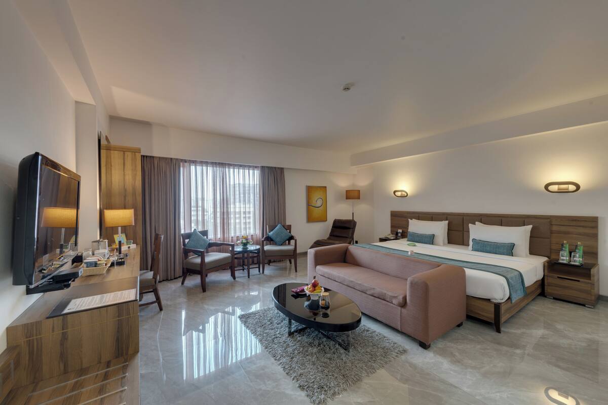 Una habitación de hotel moderna con cama, sofá, mesa de centro, televisor y escritorio con computadora.