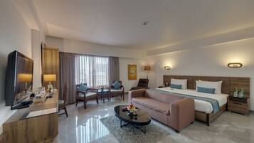 Una habitación de hotel moderna con cama, sofá, mesa de centro, televisor y escritorio con computadora.